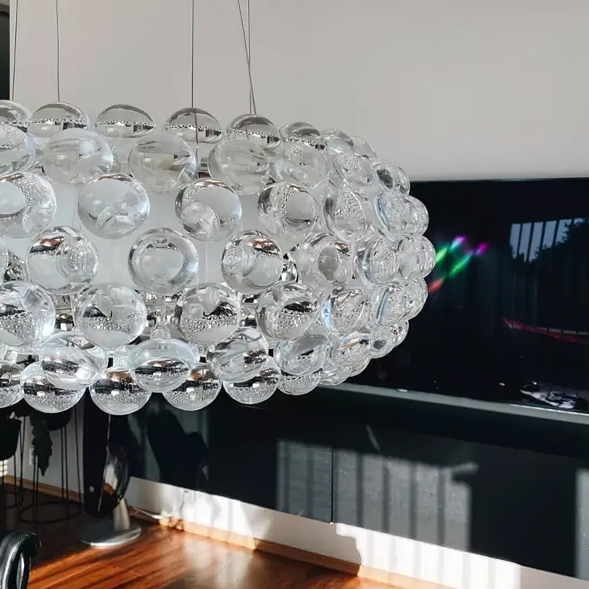 Close view of the clear acrylic spheres of this Clérachic pendant, in front of a dark screen and a white wall.