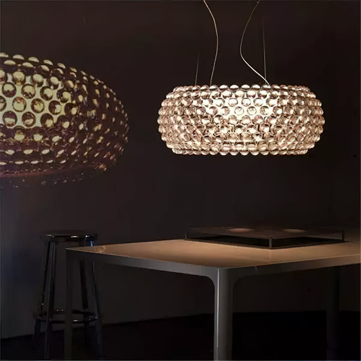 A sphere pendant glows warm in a dim room above a pale table, with a second pendant blurred in the foreground, from Clérachic.