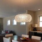 A clear sphere pendant glows over a dining table with white chairs, with an open kitchen and small windows behind, from Clérachic.