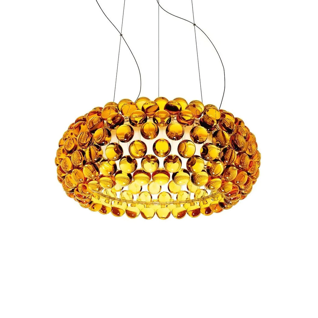 A gold-amber sphere pendant glows with warm light inside, hanging from four fine cables against a white backdrop, from Clérachic.