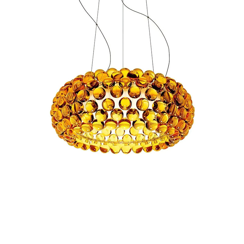 A gold-amber sphere pendant of medium size glows warm on fine cables against a white backdrop, from Clérachic.