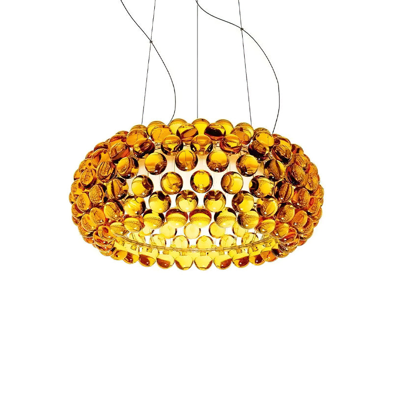 A gold-amber sphere pendant glows brightly on four fine cables against white, with a deeper orange on its outer spheres, from Clérachic.