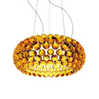 A large gold-amber sphere pendant glows warm on fine cables against a white backdrop, from Clérachic.