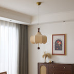 Clérachic cloud-shaped pendant light unlit in daylight, hung from its brass ceiling canopy beside sheer curtains and a walnut cabinet with a rattan cane door panel.