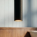 Clérachic cluster pendant light in matte black glows warm at its base beside a wooden headboard in soft daylight.