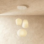 Clérachic cluster of three ribbed opal glass pendants in different shapes on one round white canopy, softly lit against limewash.