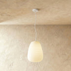 Clérachic tall egg-shaped ribbed opal glass pendant glowing softly on a thin white cord from a small white canopy.
