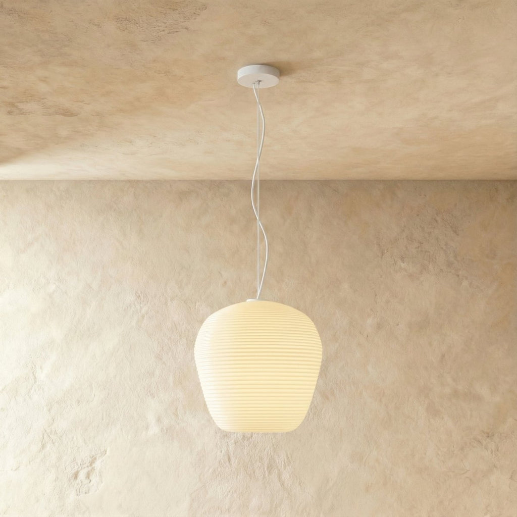 Clérachic rounded apple-shaped ribbed opal glass pendant lit warm white, hung on a thin white cord against a plaster wall.