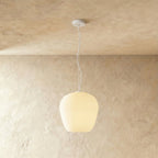 Clérachic rounded apple-shaped ribbed opal glass pendant lit warm white, hung on a thin white cord against a plaster wall.