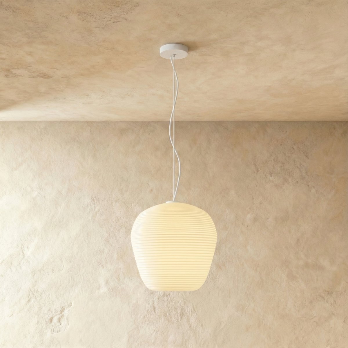 Clérachic rounded apple-shaped ribbed opal glass pendant lit warm white, hung on a thin white cord against a plaster wall.