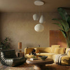 Clérachic cluster of three ribbed white glass pendants above a curved mustard sofa, round wooden table and leather lounge chair.