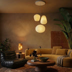 Clérachic three ribbed glass pendants glowing warm in a dim living room with a mustard sofa, leather armchair and tall plant.