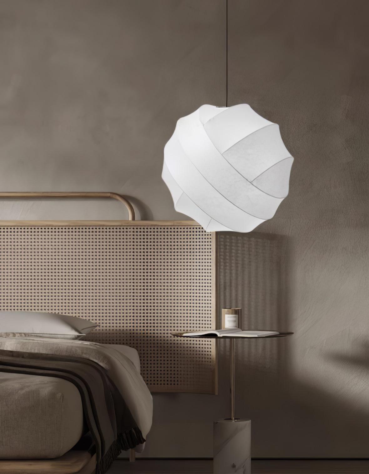 Clérachic globe pendant light lit beside a caned rattan headboard, above a slim side table on a marble base holding a candle and an open book.