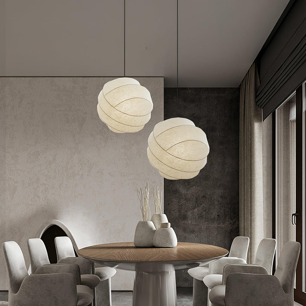 Clérachic globe pendant lights, a staggered pair above a round wood table, framed wide to show the full ring of curved dining chairs.