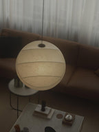Clérachic pendant light photographed at night above a brown leather sofa, a smooth banded globe shade with a metal collar where the cord enters the top.