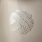 Clérachic globe pendant light in an angled close-up against a warm beige wall, lit so the fibre glows and the parting between two bands burns brighter.