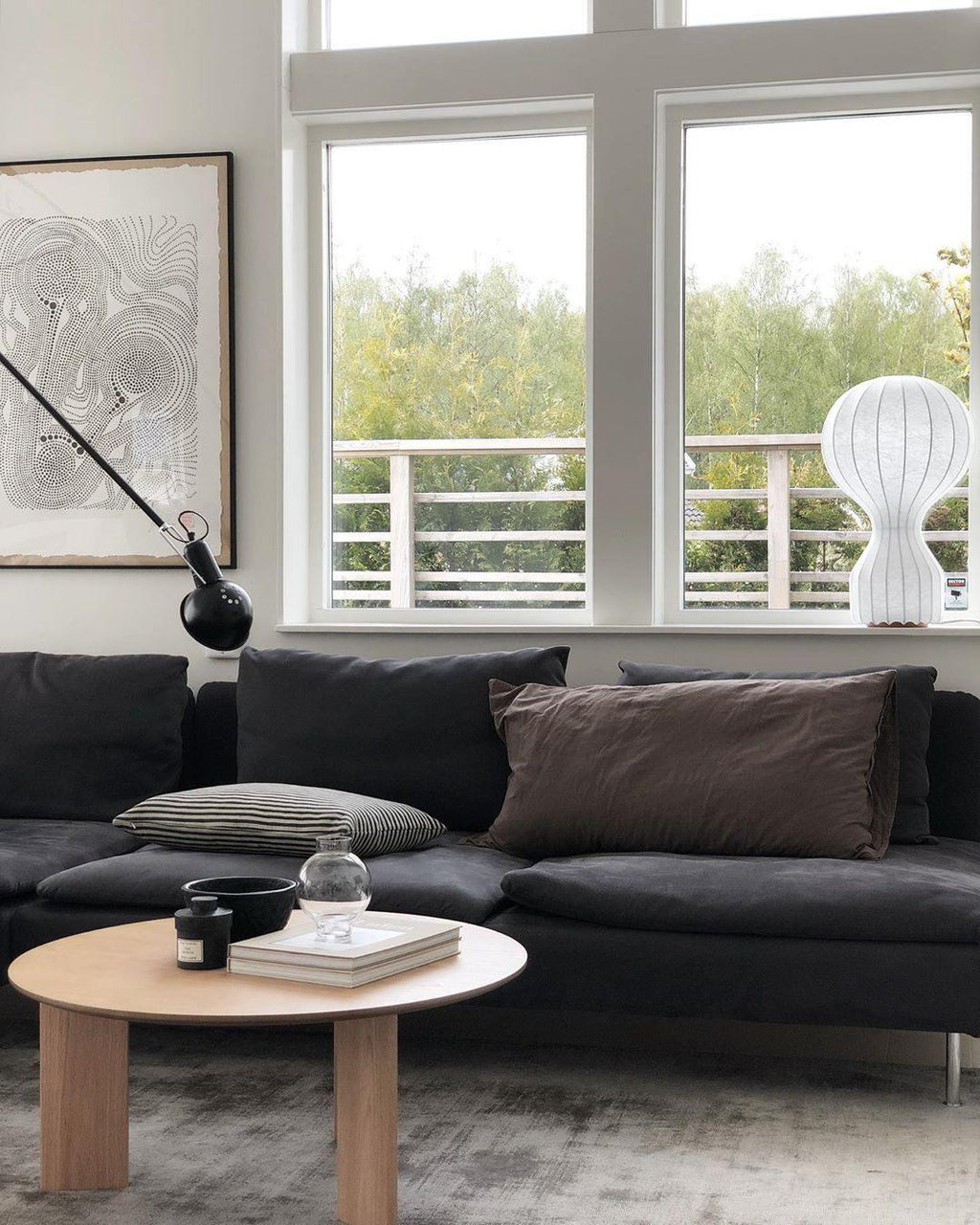 A small Clérachic lamp on a balcony-side shelf behind a dark sofa, with a round wooden coffee table in the foreground.