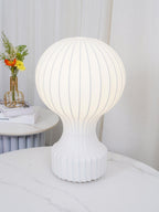 Close view of the lit Clérachic lamp on a marble table, its shade glowing evenly with fine ribs, and curtains behind.