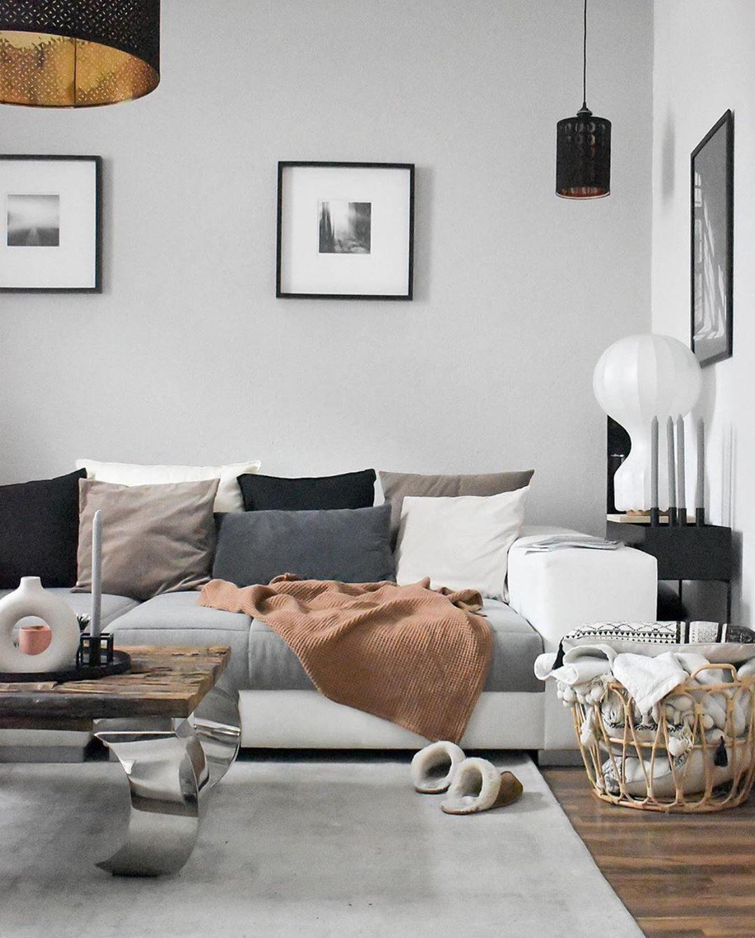 Clérachic lamp in the corner of a grey living room, behind a sofa with a tan throw and sheepskin slippers on the rug.