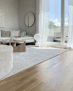 A small Clérachic lamp by a tall balcony door in a bright living room, with a round wooden coffee table and a pale rug.