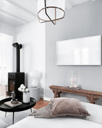 Clérachic lamp on a low stool next to a black wood-burning stove, with a framed screen and a dusty-pink cushion.