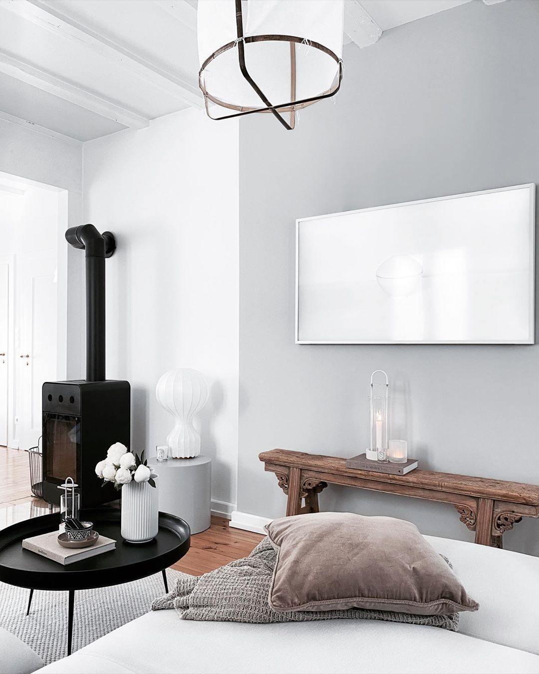 Clérachic lamp on a low stool next to a black wood-burning stove, with a framed screen and a dusty-pink cushion.