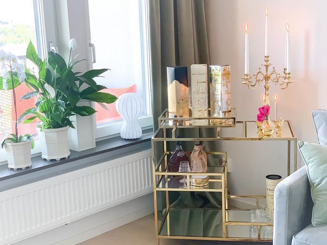 Small Clérachic lamp on a windowsill, beside a peace lily and a gold bar cart with candles and bottles.