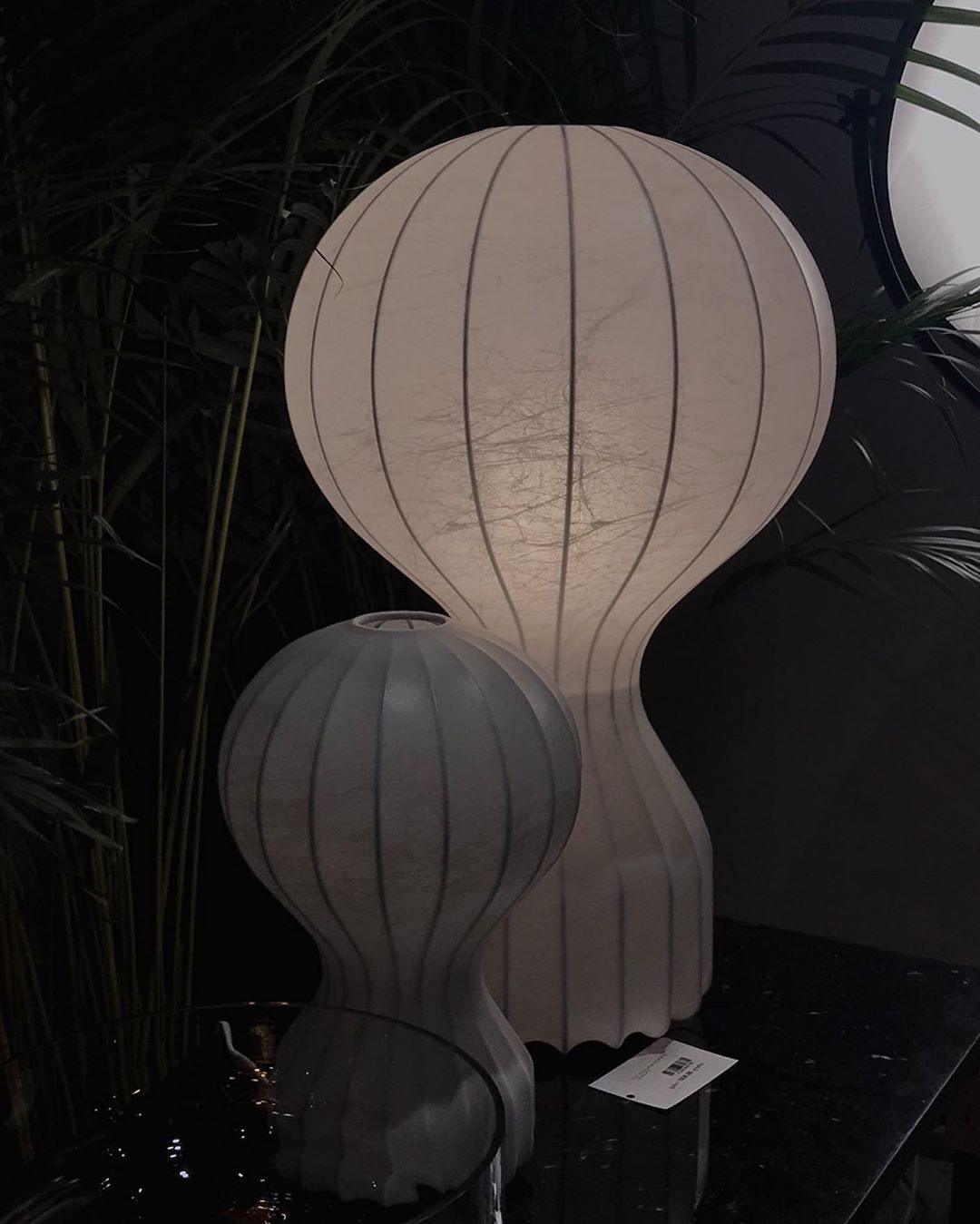 Two sizes of the Clérachic lamp in a dim showroom with palms behind, a small price tag at the foot of the larger lamp.