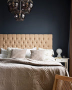 A bedside Clérachic lamp on a white nightstand in front of a navy wall, with a tufted headboard and a smoked-glass pendant.