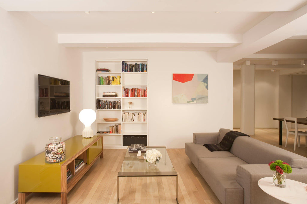 Small Clérachic lamp on a yellow low cabinet in a large open-plan living room with a pale sofa and a bookcase.