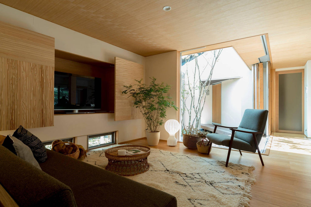 A distant, lit Clérachic lamp on the floor of a timber-panelled living room, with a green armchair and a woven rug.