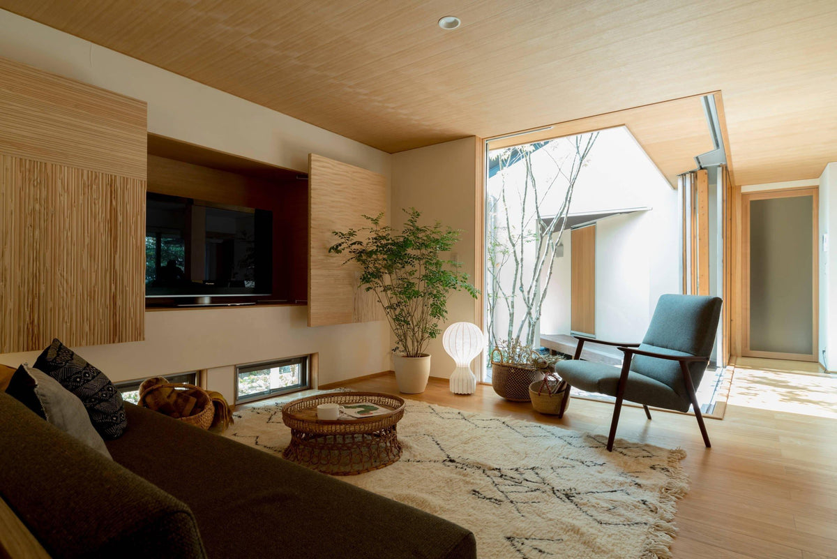 A distant, lit Clérachic lamp on the floor of a timber-panelled living room, with a green armchair and a woven rug.