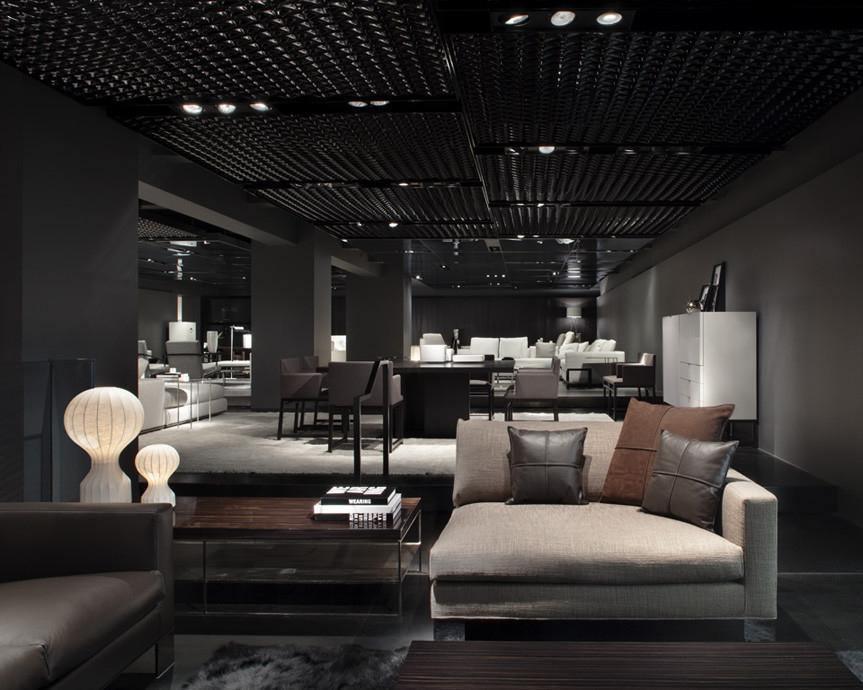 Two sizes of the Clérachic lamp on low tables in a dark, modern showroom with a grid ceiling and a beige sofa.