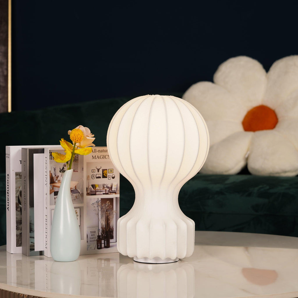 Lit Clérachic table lamp on a white marble table, in front of a green velvet sofa with a white flower-shaped cushion.