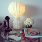 Warm light from a Clérachic table lamp on a glass table, beside white roses, an old black telephone and a pile of art books.