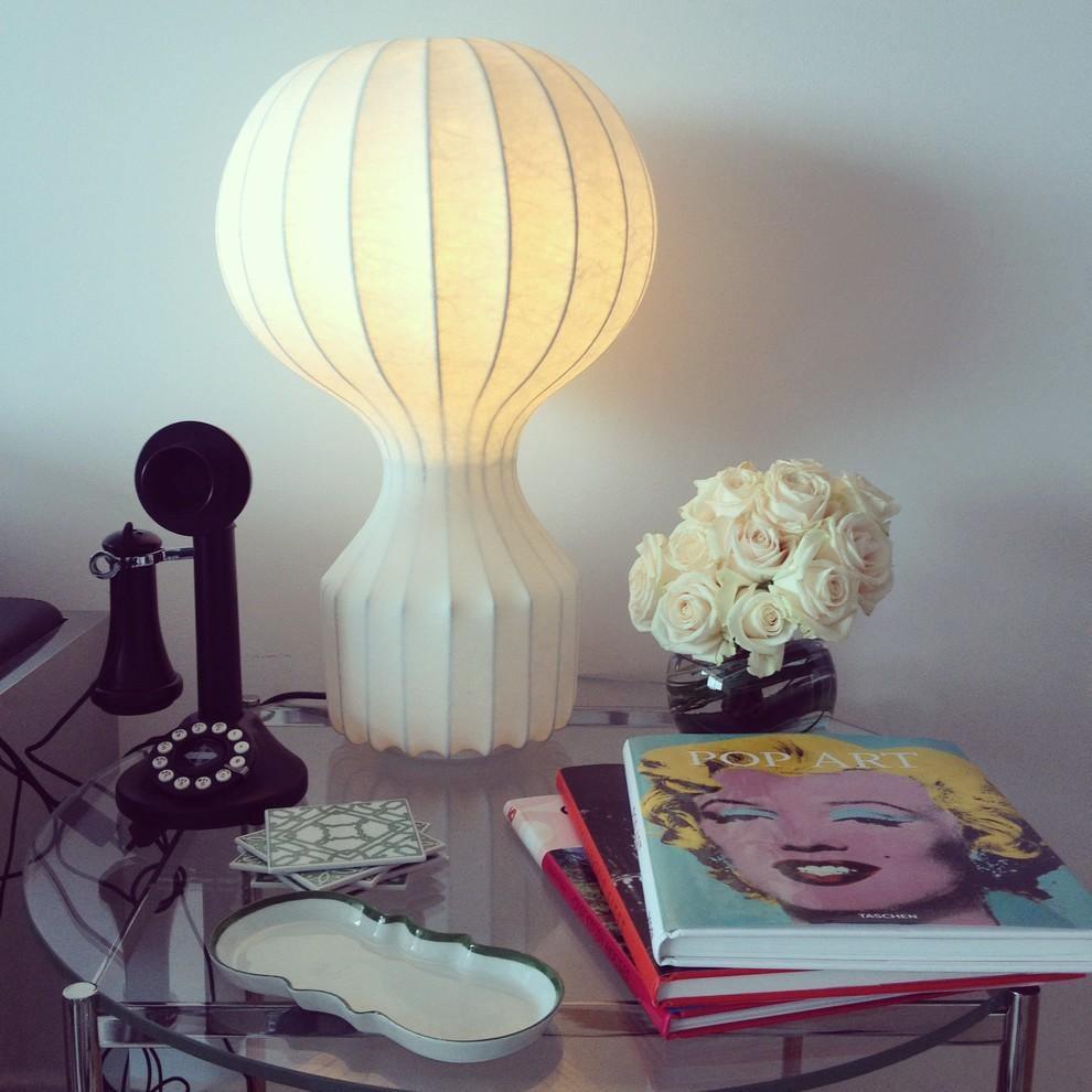 Warm light from a Clérachic table lamp on a glass table, beside white roses, an old black telephone and a pile of art books.
