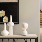Small Clérachic table lamp on a stone-topped console, next to three tall white vases and a dark framed print.
