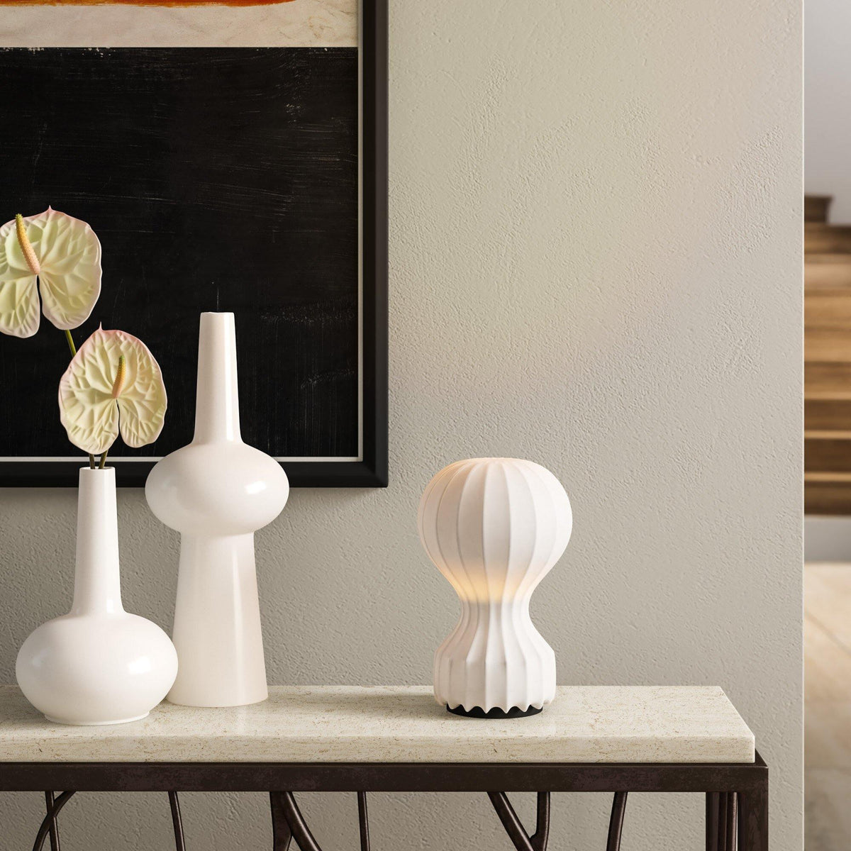 Small Clérachic table lamp on a stone-topped console, next to three tall white vases and a dark framed print.