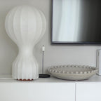 Tall Clérachic lamp on a white sideboard beneath a wall-mounted TV, next to a beaded stone bowl and a slim black candlestick.