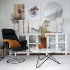 A pair of Clérachic lamps in the background of a bright living room, with a black lounge chair and a round marble coffee table.