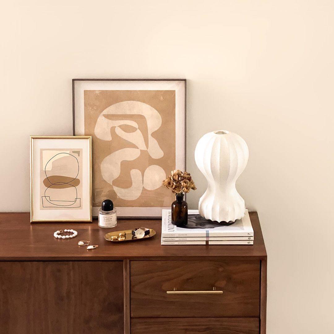 Clérachic table lamp on a walnut chest of drawers, beside two framed abstract prints and a small tray of jewellery.