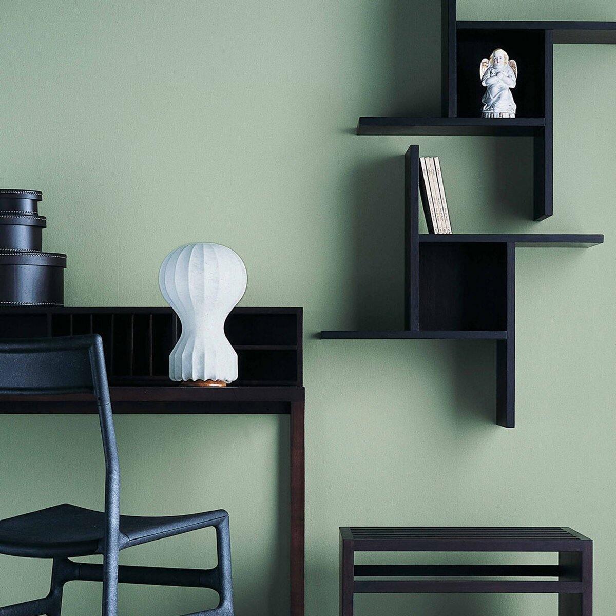 Small Clérachic lamp on a black desk against a sage-green wall, with dark shelving and a black chair in view.