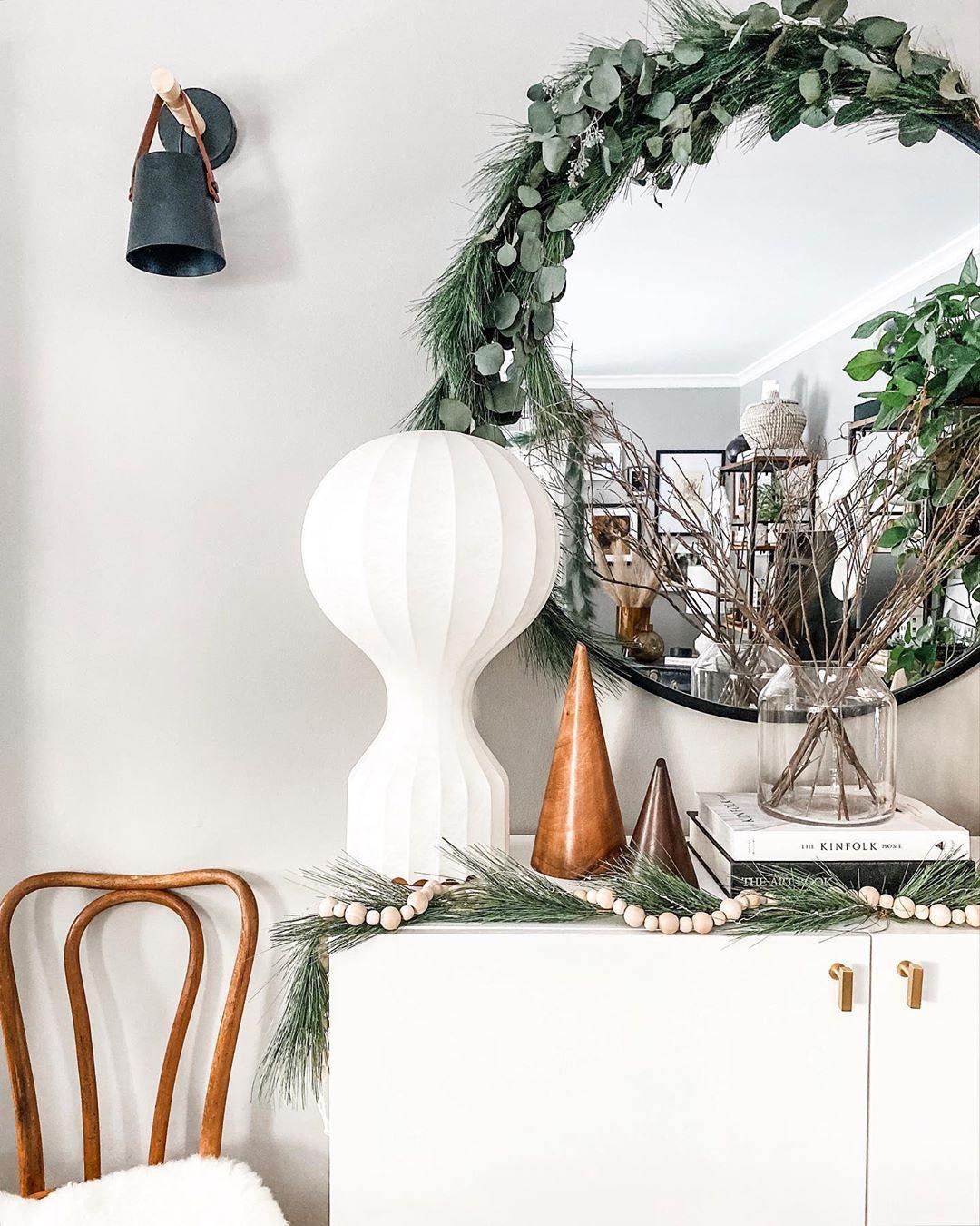 Tall Clérachic lamp on a white cabinet at Christmas, beside a eucalyptus wreath, a round mirror and a copper cone.
