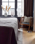 Distant Clérachic lamp on a bedroom windowsill, next to pampas grass in a white vase, with a rattan armchair below.