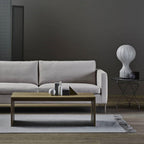 Clérachic lamp on a small side table behind a grey sofa, in a living room with a dark wall and a wooden coffee table.