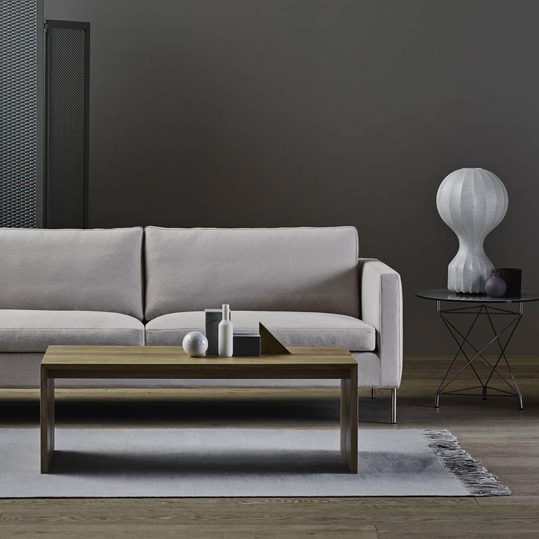 Clérachic lamp on a small side table behind a grey sofa, in a living room with a dark wall and a wooden coffee table.