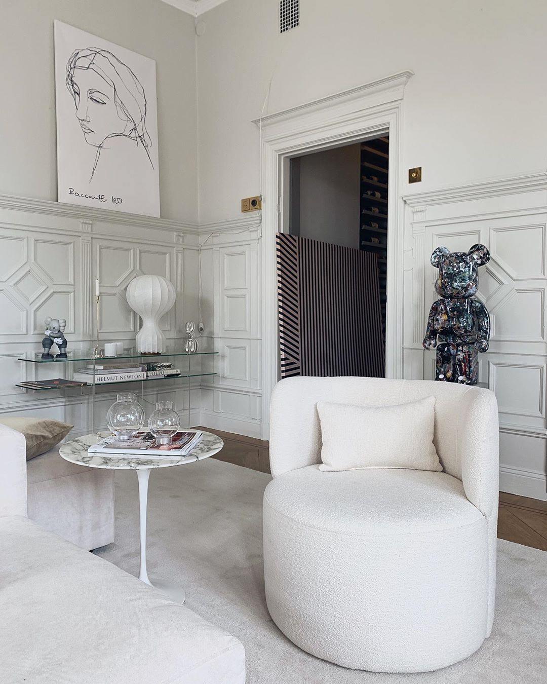 Small Clérachic lamp on a glass shelf in a tall white panelled room, with a white bouclé chair in the foreground.