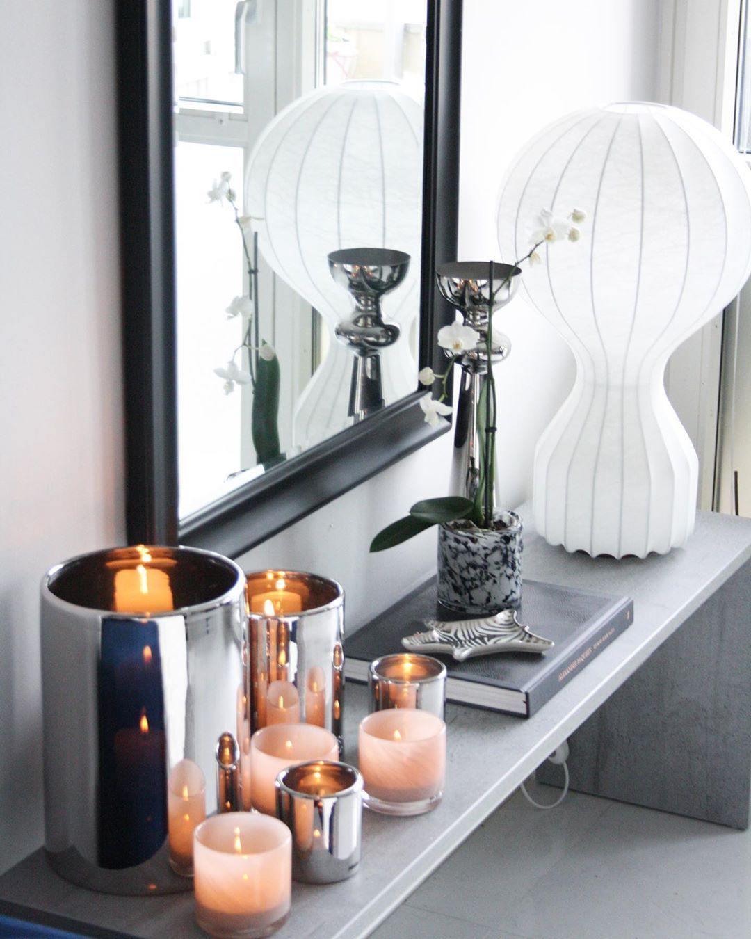 Larger Clérachic lamp on a dark ledge beside a window, with mirrored silver candle holders and flickering tea lights below it.