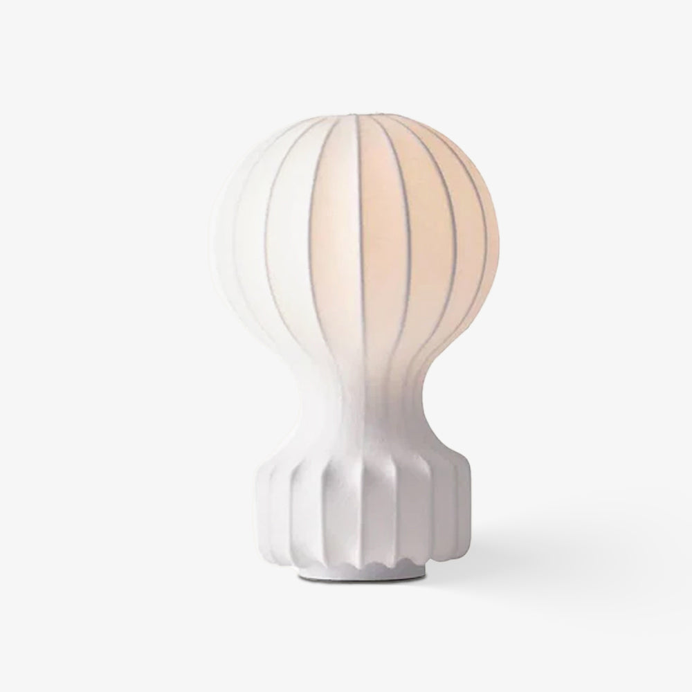 Clérachic table lamp glowing softly on a plain pale backdrop, the ribbed white shade showing a warm inner light.