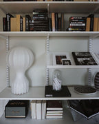 Clérachic table lamp on an open white shelf among rows of books, a glass cloche and an old speaker.
